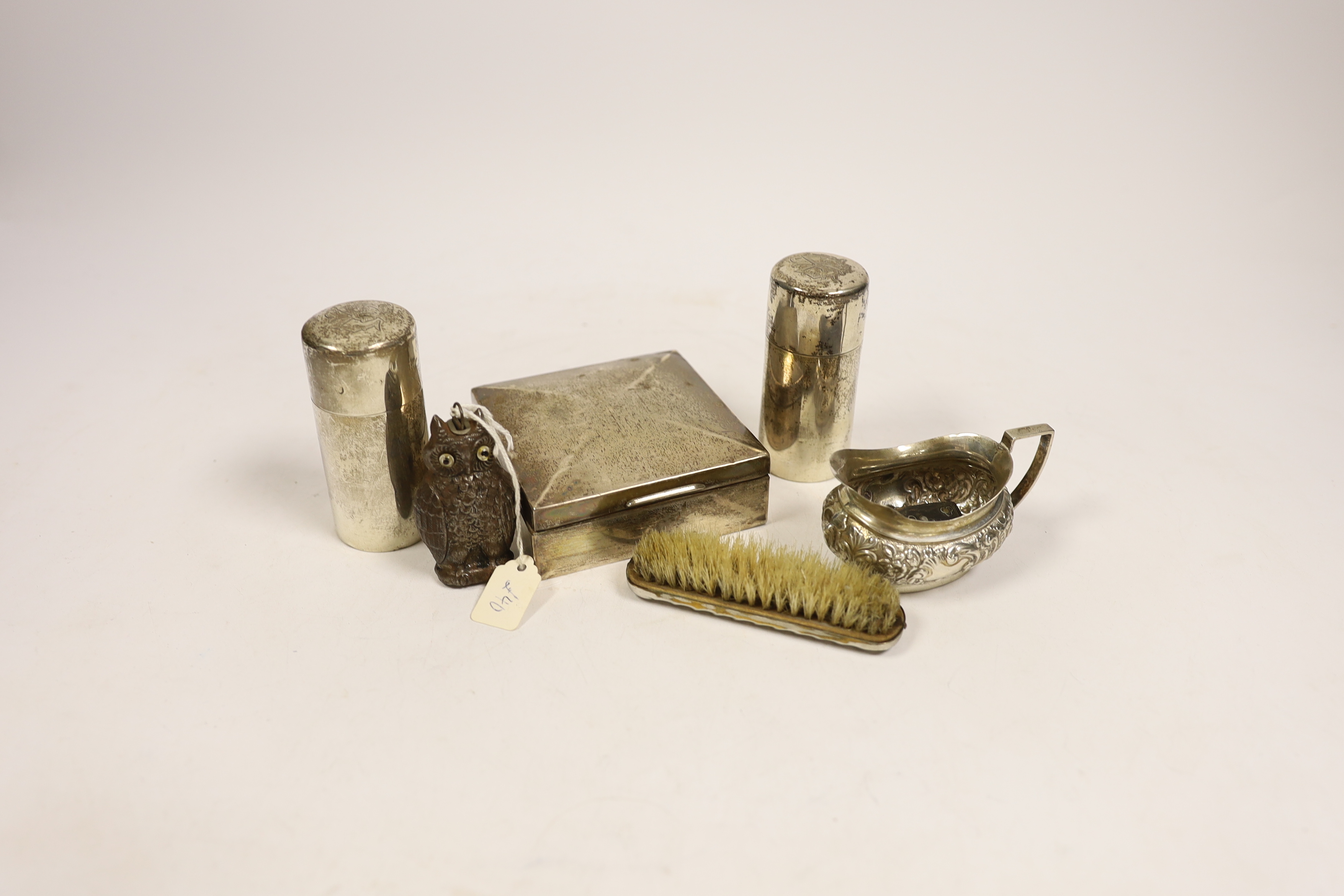 A late Victorian embossed silver cream jug, a pair of silver toilet bottles, a silver backed brush, a silver cigarette box and two other items.